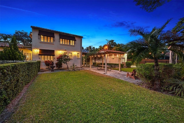 back house at dusk with a patio area, a pergola, and a yard