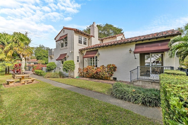 back of house featuring stucco siding, a yard, a chimney, and a tiled roof