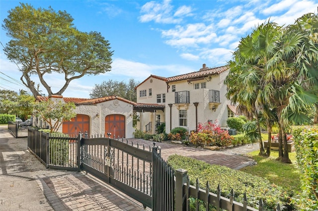 mediterranean / spanish-style house with stucco siding, a gate, a fenced front yard, a balcony, and a tiled roof