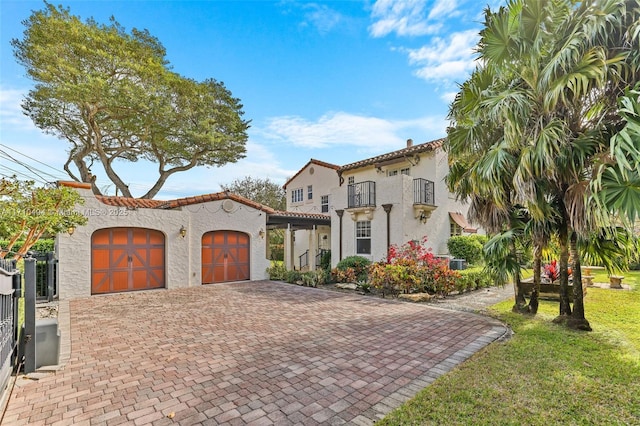 mediterranean / spanish home featuring a front yard, a balcony, an attached garage, stucco siding, and decorative driveway