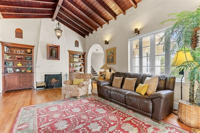 living room featuring arched walkways, wooden ceiling, beamed ceiling, light wood-type flooring, and a large fireplace