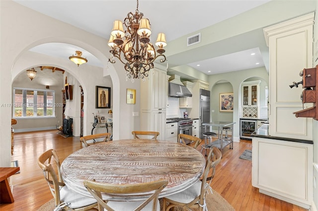 dining area featuring light wood finished floors, visible vents, beverage cooler, arched walkways, and a notable chandelier