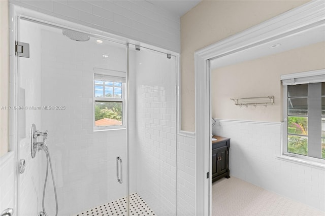 bathroom featuring a wainscoted wall, tile walls, a stall shower, and vanity