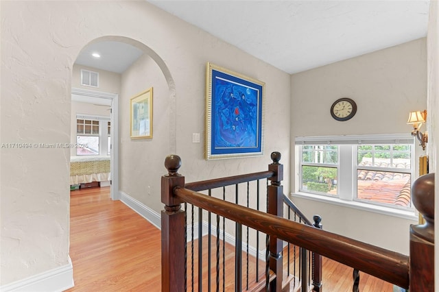 hall with an upstairs landing, visible vents, light wood finished floors, and baseboards