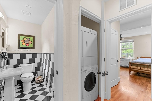 laundry room with visible vents, light floors, stacked washing maching and dryer, and tile walls