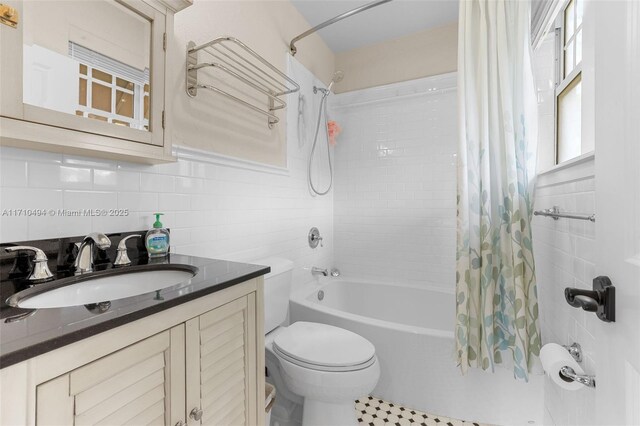 full bath featuring vanity, shower / bath combination with curtain, tile walls, toilet, and backsplash