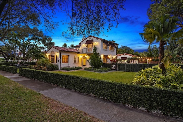 mediterranean / spanish-style house featuring fence, a tile roof, stucco siding, a yard, and a balcony