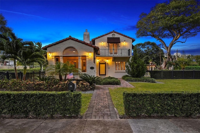 mediterranean / spanish-style house featuring a front yard, a balcony, fence, a chimney, and a tiled roof