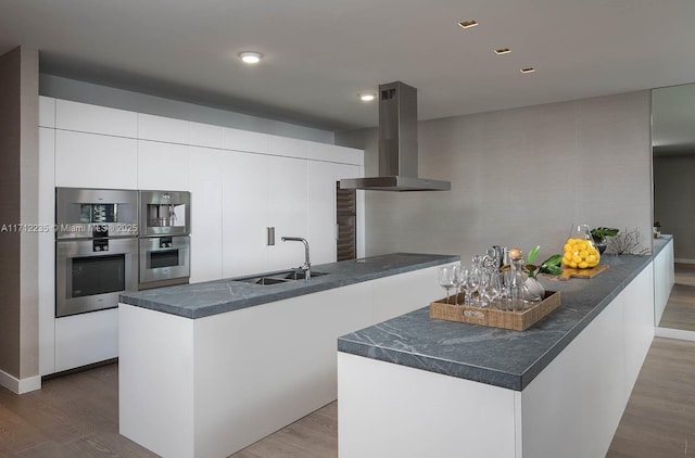 kitchen featuring white cabinets, dark countertops, modern cabinets, island exhaust hood, and a sink