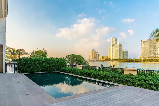 view of swimming pool with a water view, fence, and a city view