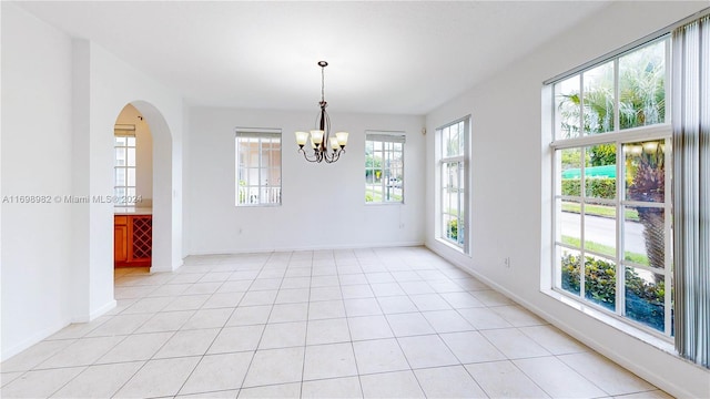 tiled empty room featuring a notable chandelier and a healthy amount of sunlight