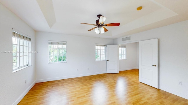 empty room featuring ceiling fan, light hardwood / wood-style floors, and a tray ceiling