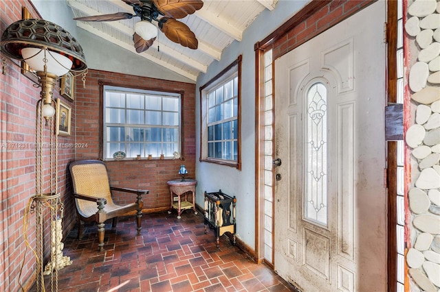 foyer featuring plenty of natural light, ceiling fan, brick wall, and vaulted ceiling