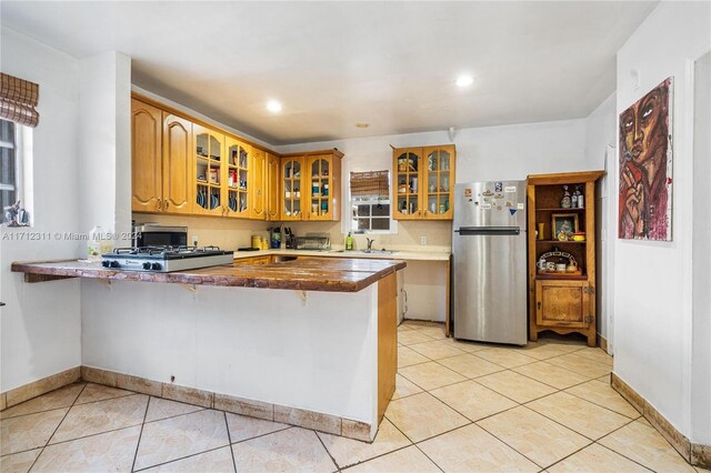 kitchen with sink, light tile patterned floors, a kitchen bar, kitchen peninsula, and stainless steel refrigerator