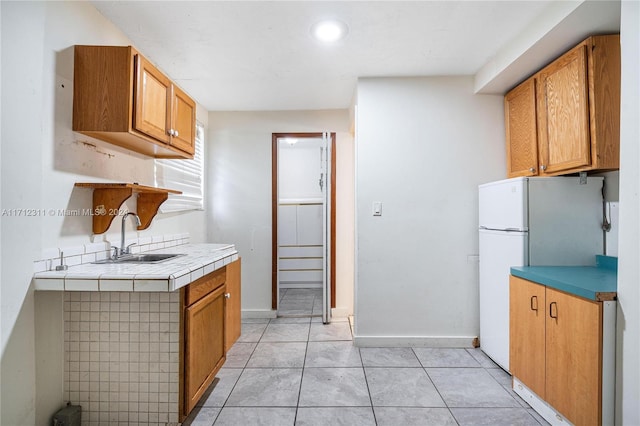 kitchen with tile counters, white refrigerator, light tile patterned floors, and sink