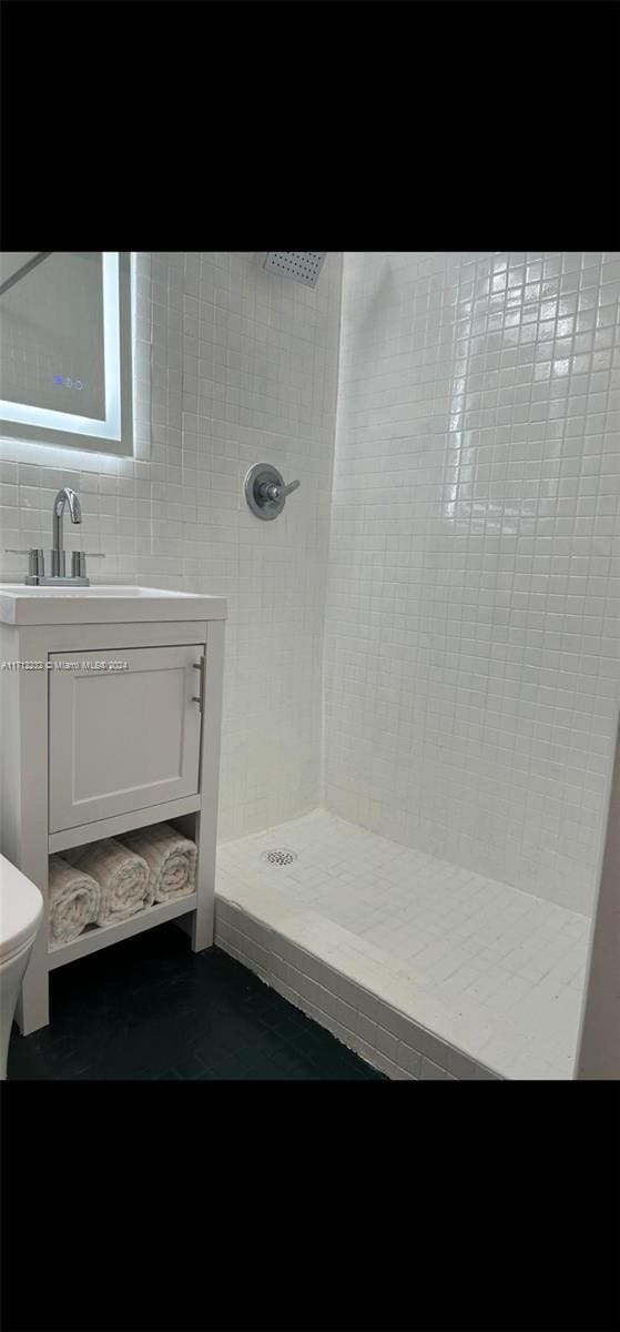 bathroom featuring vanity, toilet, a tile shower, and tile walls