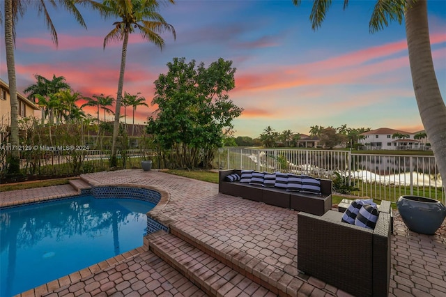 pool at dusk with a patio, a water view, and an outdoor hangout area