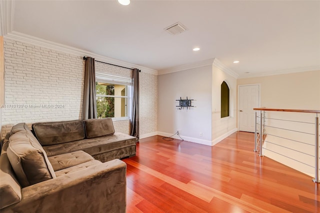 living room featuring wood-type flooring, ornamental molding, and brick wall