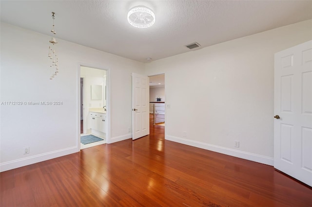 unfurnished bedroom with hardwood / wood-style floors, a textured ceiling, and ensuite bath