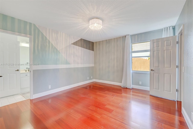 empty room with wood-type flooring and a notable chandelier