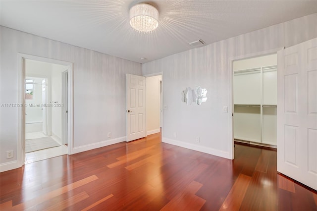 unfurnished bedroom with dark hardwood / wood-style floors, a spacious closet, and an inviting chandelier