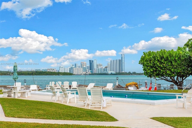 view of swimming pool featuring a water view, a patio area, and a lawn