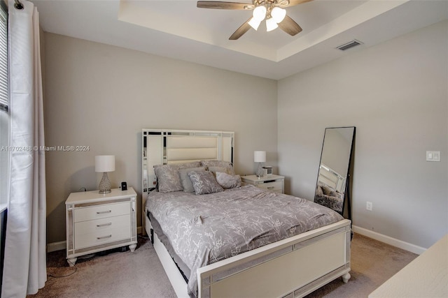 bedroom with ceiling fan, a raised ceiling, and light carpet