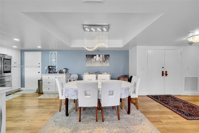 dining area with light wood-type flooring, a raised ceiling, and a notable chandelier