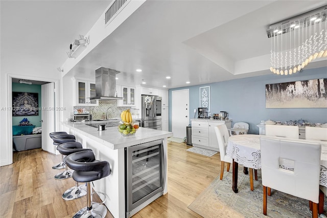 kitchen featuring stainless steel fridge, wall chimney exhaust hood, beverage cooler, light hardwood / wood-style floors, and white cabinetry