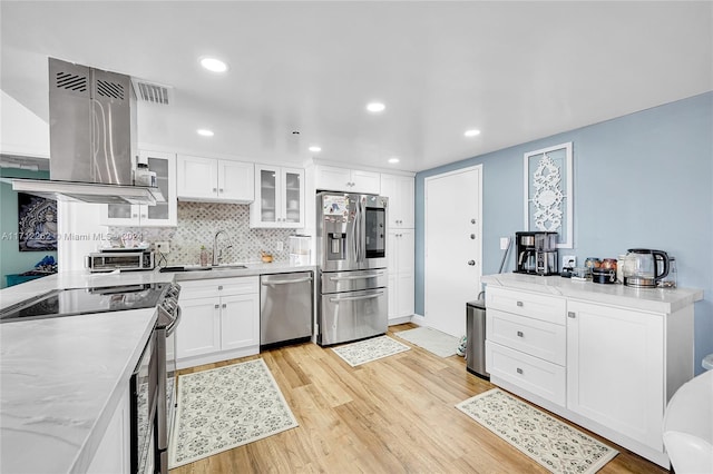 kitchen with exhaust hood, light wood-type flooring, tasteful backsplash, white cabinetry, and stainless steel appliances