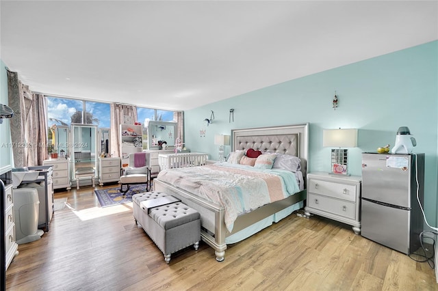 bedroom with light hardwood / wood-style flooring, stainless steel refrigerator, and a wall of windows