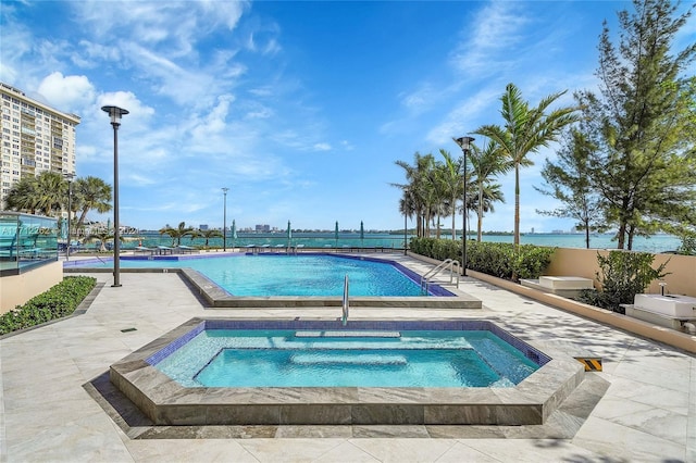 view of swimming pool with a patio, a water view, and a hot tub