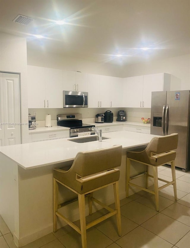 kitchen with a kitchen breakfast bar, light tile patterned floors, stainless steel appliances, and white cabinetry