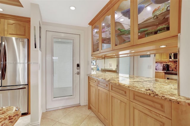 kitchen featuring backsplash, light stone countertops, light tile patterned floors, light brown cabinetry, and stainless steel appliances