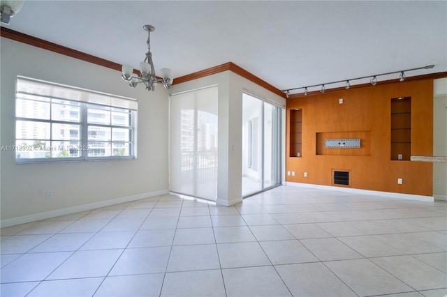 empty room featuring built in shelves, ornamental molding, a chandelier, and light tile patterned flooring