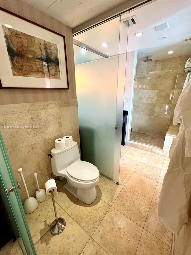 bathroom with a tile shower, tile walls, and toilet