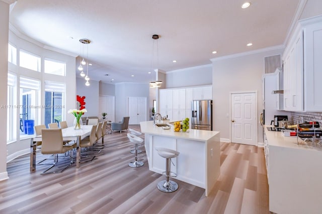 kitchen featuring white cabinets, hanging light fixtures, stainless steel fridge, an island with sink, and tasteful backsplash