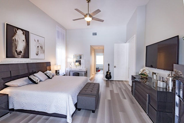 bedroom with ceiling fan, light hardwood / wood-style flooring, and a high ceiling