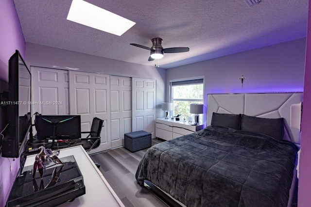 bedroom with hardwood / wood-style floors, ceiling fan, a textured ceiling, and a skylight