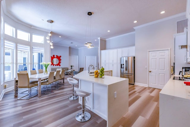 kitchen featuring stainless steel refrigerator with ice dispenser, light wood-type flooring, white cabinetry, and pendant lighting