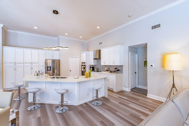 kitchen featuring a kitchen island with sink, a breakfast bar area, wall chimney exhaust hood, white cabinetry, and stainless steel appliances