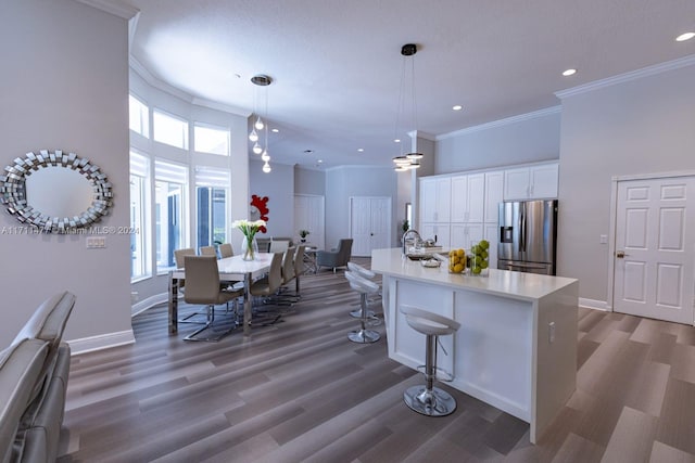 kitchen with plenty of natural light, stainless steel fridge, white cabinetry, and a kitchen island with sink