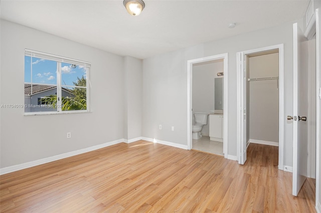 unfurnished bedroom featuring a closet, a spacious closet, connected bathroom, and light hardwood / wood-style flooring