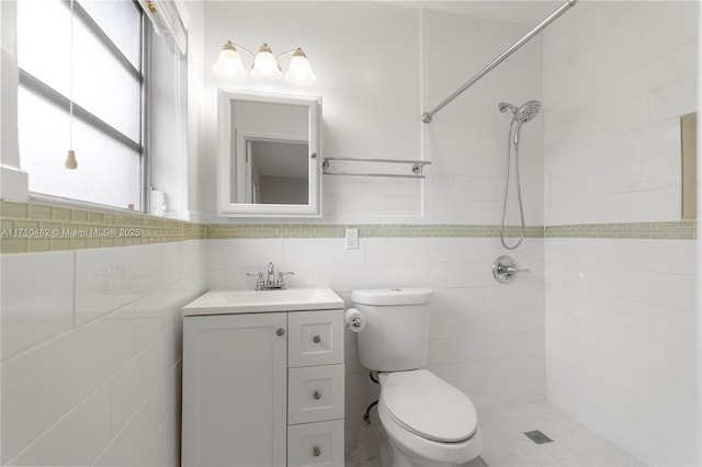 bathroom with tile walls, toilet, tiled shower, and vanity