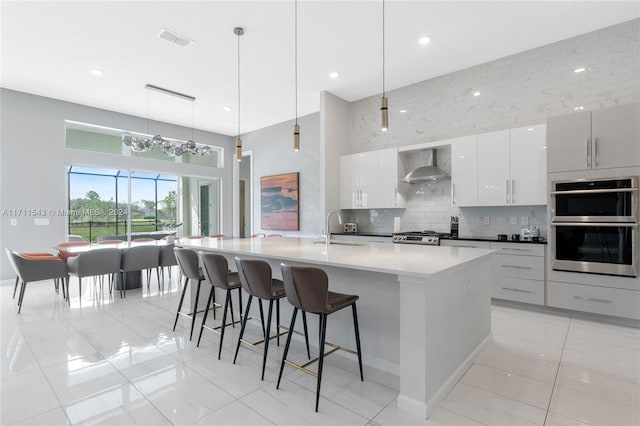 kitchen featuring pendant lighting, white cabinetry, wall chimney exhaust hood, and a large island