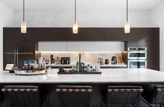 kitchen featuring decorative light fixtures, a kitchen bar, stainless steel double oven, and tasteful backsplash