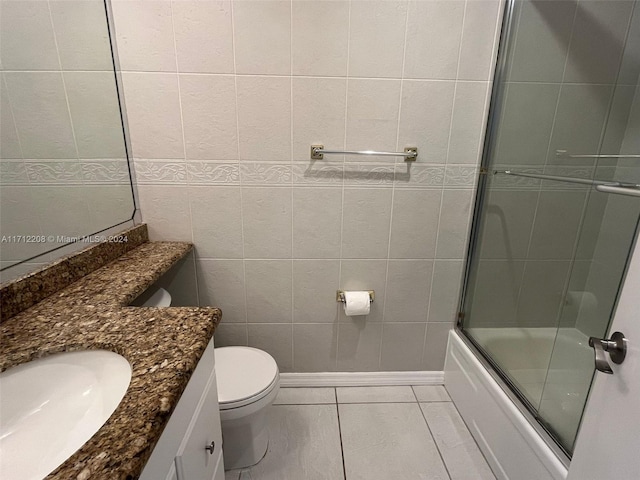 full bathroom with tile patterned floors, toilet, shower / bath combination with glass door, vanity, and tile walls