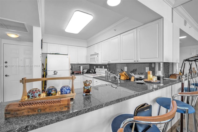 kitchen featuring a breakfast bar, white appliances, kitchen peninsula, dark stone countertops, and white cabinetry