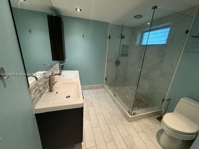 bathroom featuring a shower with door, vanity, and toilet