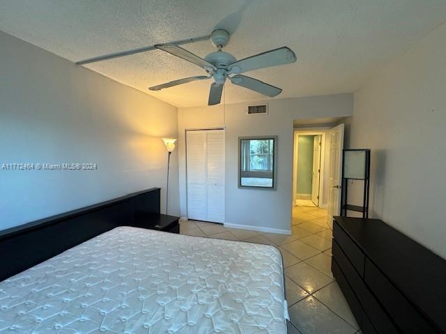 bedroom with ceiling fan, light tile patterned flooring, a textured ceiling, and a closet